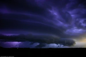 The shelf cloud of an encroaching thunderstorm in rural Iowa is backlit purple by lightning from within.