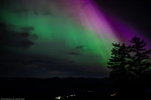Purple and green auroras shimmer over the dark mountain landscape above Troy, Montana.