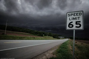 Suggesting it might apply more to the wind than the roads, a sign dominates the highway shoulder while a thunderstorm looms darkly on the horizon. Rural Nebraska, just over the border with Iowa.
