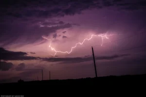 Lightning arcs from a cloud base in rural Nebraska, with subtle fireflies in the foreground.