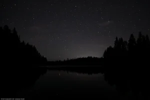 A starry night sky glitters above the calm, glassy waters of Alvord Lake in northwestern Montana.